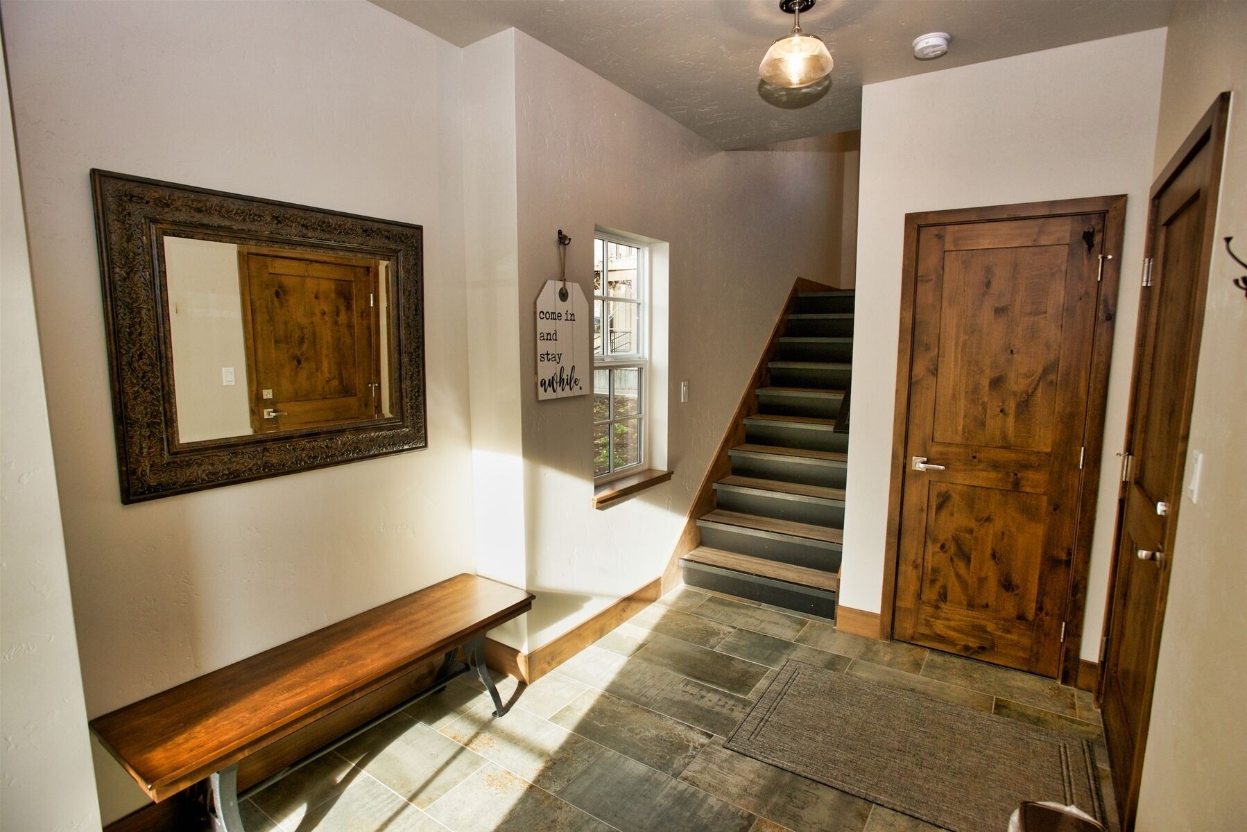 A hallway with a wooden bench, a mirror, a staircase, and a wooden door.