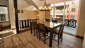 A dining area with a wooden table and chairs, a chandelier, and a view of a building through a glass door. - Suite Retreat: Short Walk to Downtown McCall, A/C, Propane Fireplace (McCall)