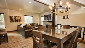 A spacious living room with a large dining table, leather sofa, and a TV mounted on the wall. - Suite Retreat: Short Walk to Downtown McCall, A/C, Propane Fireplace (McCall)