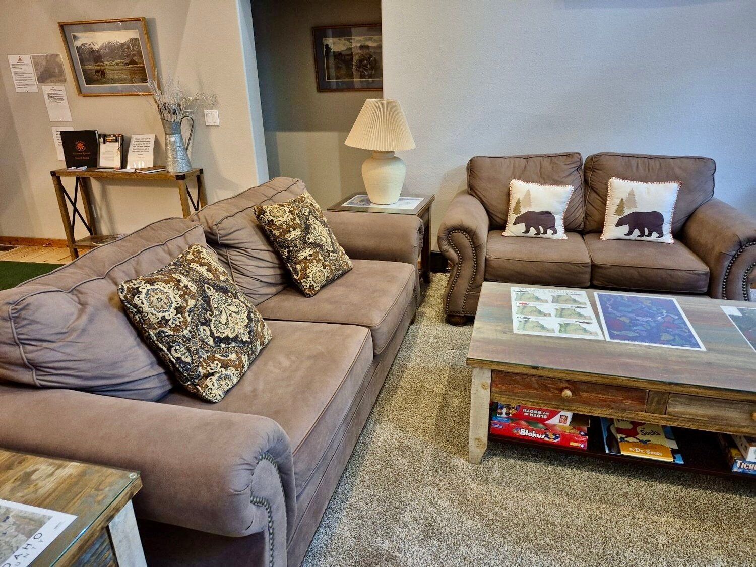 A living room with two brown leather sofas, patterned cushions, a wooden coffee table with books, and a lamp.