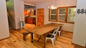 A dining area with a wooden table and chairs, a chandelier, and a view of the kitchen and living area. - Peace in the Pines: Woodland Oasis in Spring Mountain Ranch, Private Hot Tub (McCall)