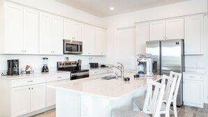 A modern kitchen with white cabinets, stainless steel appliances, a central island with bar stools, and a built-in oven.