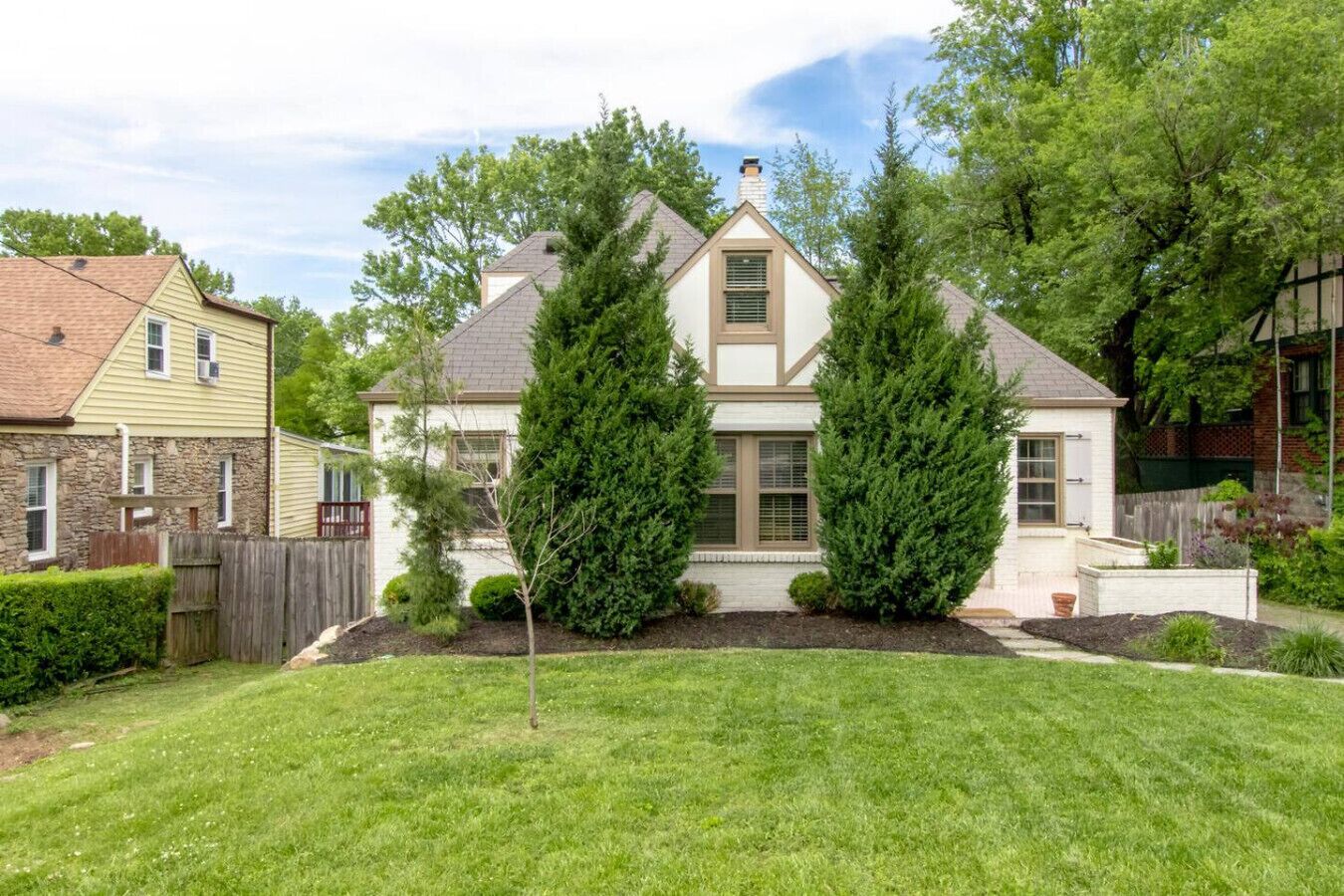 A two-story house with a front yard, a stone foundation, and a fenced backyard.