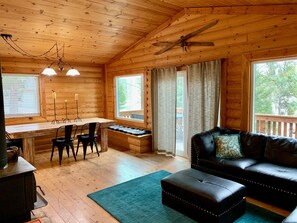 A cozy cabin interior with a wooden dining table, chairs, a black leather sofa, and a fireplace.