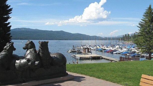 Un puerto deportivo con barcos amarrados, una estatua de caballos y una vista despejada de montañas al fondo.