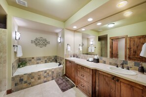 Une salle de bain avec une baignoire, deux lavabos, des meubles en bois et un grand miroir.