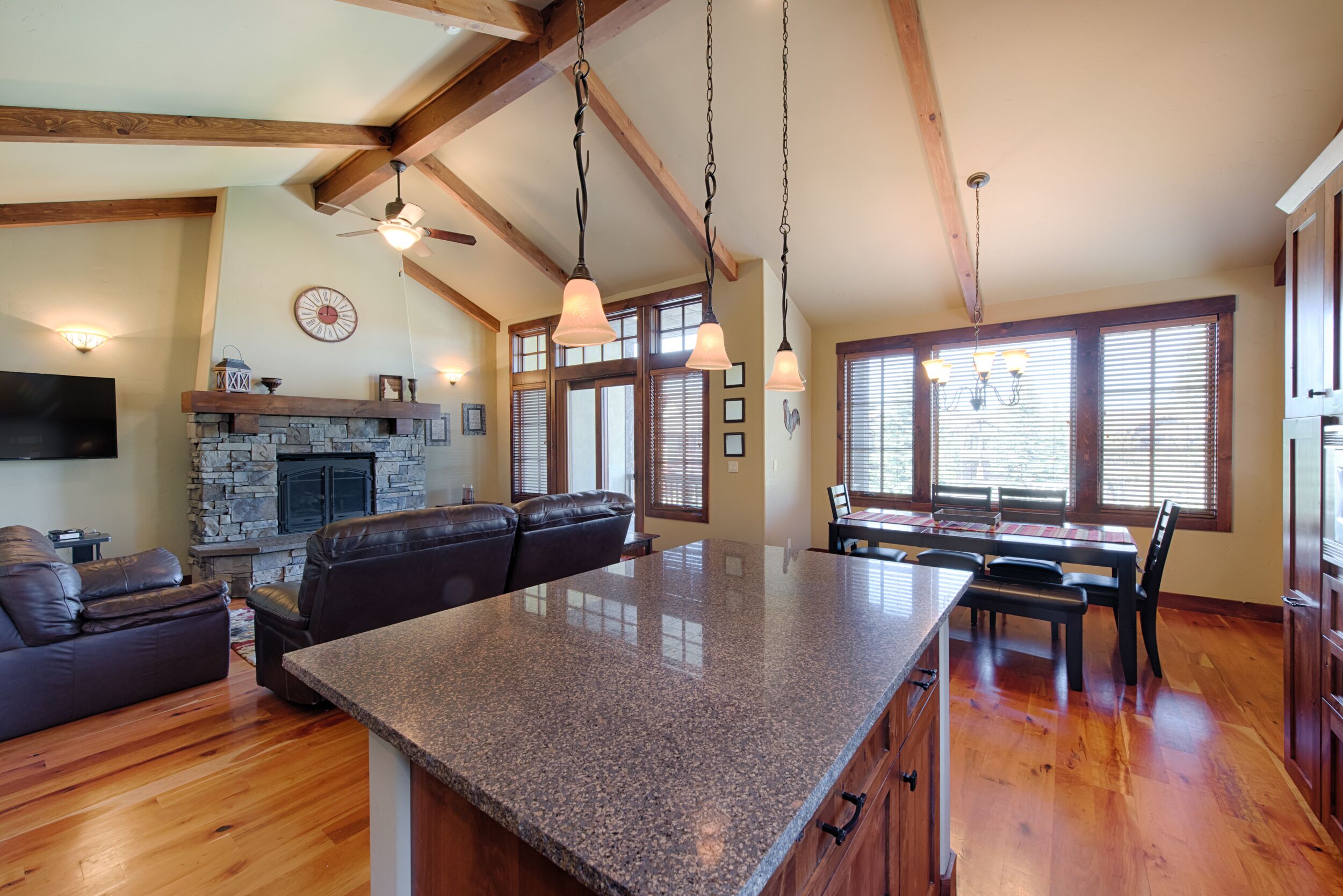 A spacious living area with a large island, wooden beams, a stone fireplace, and a dining area with a table and chairs.