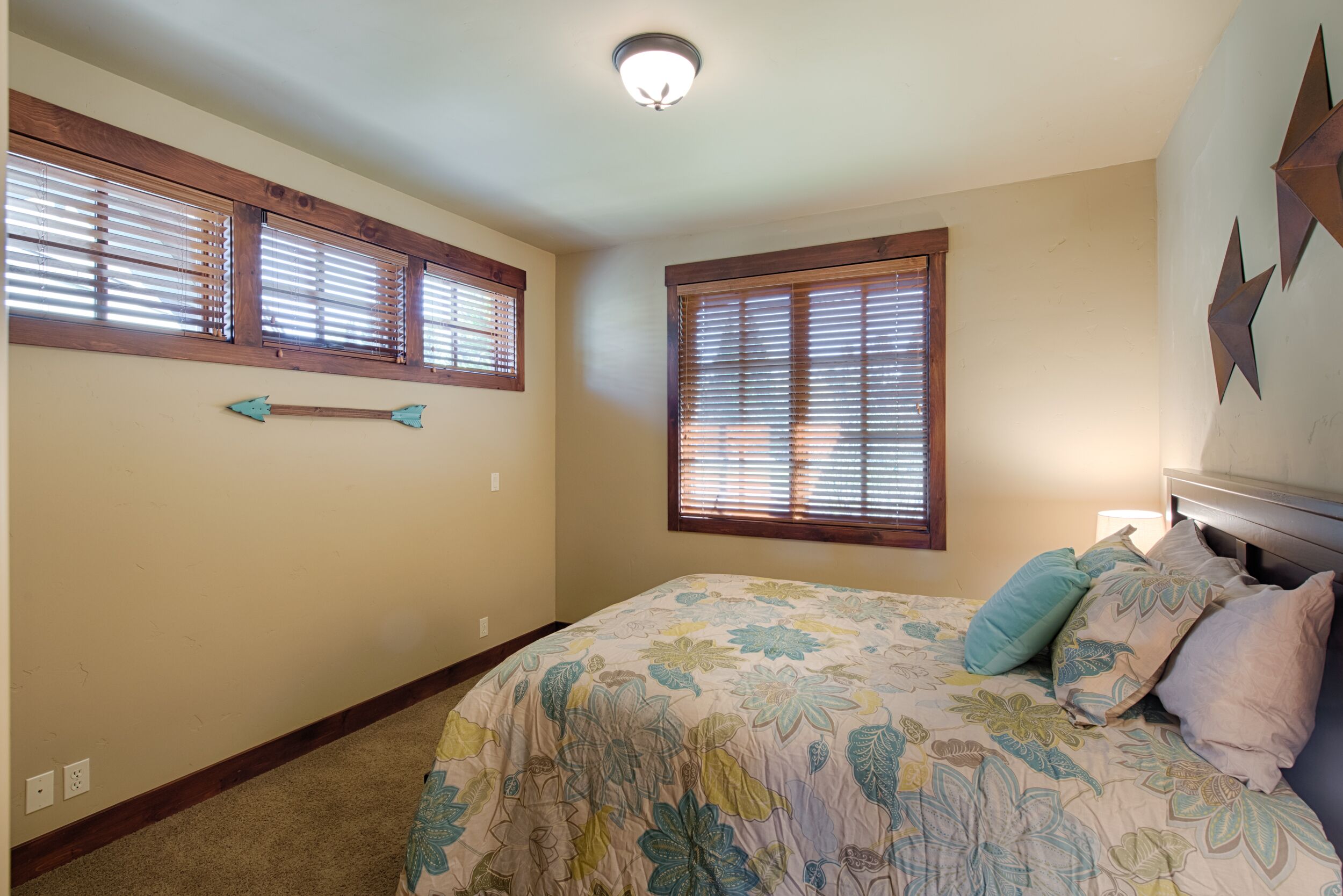 A bedroom with a floral bedspread, wooden window frames, and a ceiling light fixture.