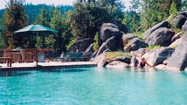 A pool area with large rocks, a wooden deck, and a green umbrella.