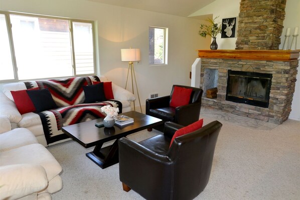 A living room with a stone fireplace, a white couch, a black leather chair, and a coffee table. - Downtown Lakeview Villa Townhome: Walk to Lake and Downtown, Lakeview Balcony (McCall)