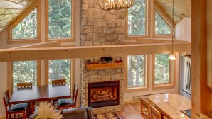 Una cabaña espaciosa con chimenea de piedra, comedor de madera y grandes ventanales con vistas al bosque.