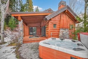 Une cabane en rondins dotée d’un jacuzzi, de murs en pierre et d’une terrasse en bois.