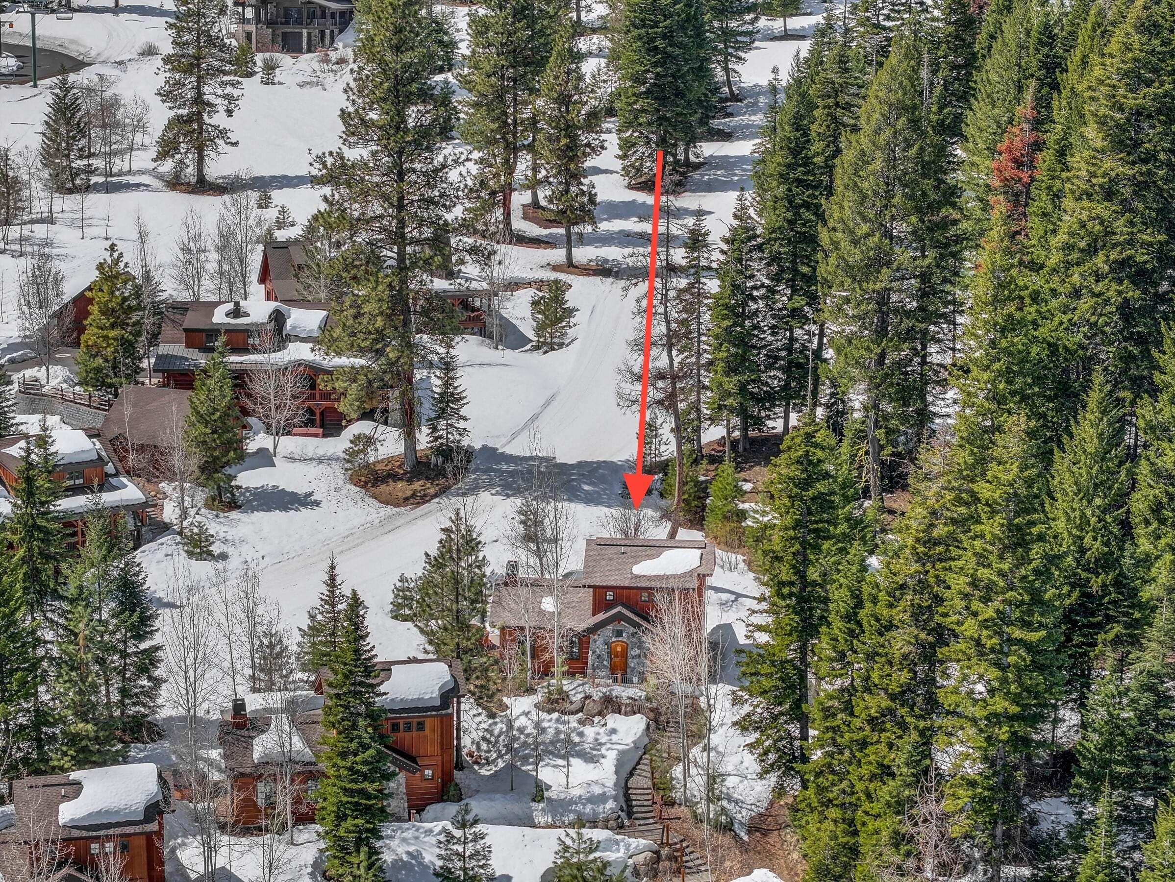 Una cabaña nevada con varias cabañas, un edificio central con techo rojo y una pista de esquí.