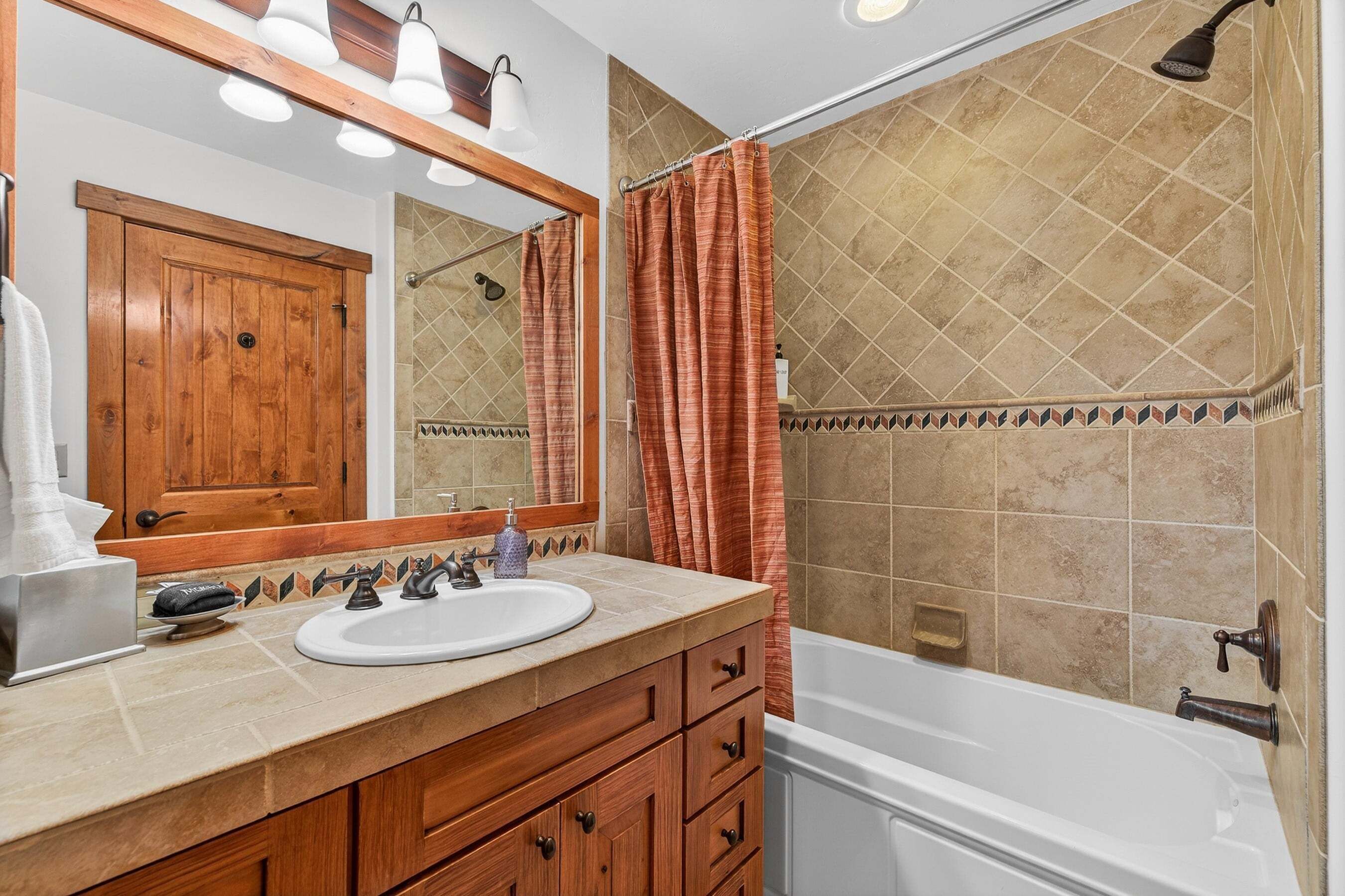 A bathroom with a wooden vanity, a sink, a mirror, a shower curtain, and a bathtub.