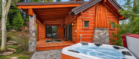 Una cabaña de troncos con jacuzzi, mobiliario exterior y un muro de piedra.