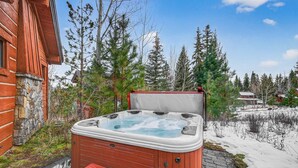 Eine Holzhütte mit Whirlpool, umgeben von Bäumen und einer verschneiten Landschaft.