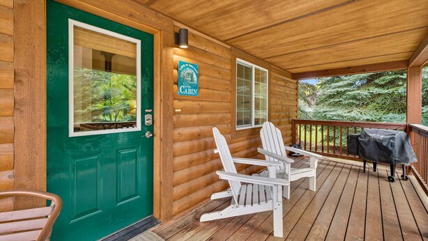 A wooden cabin with a green door, two Adirondack chairs, a barbecue grill, and a sign that reads 'The Cabin.' - Hubbard Cabin in McCall - near Payette Lake, private hot tub, quiet (McCall)