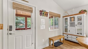 A room with a white door, a bench, a cabinet with glass doors, and a window with a view of trees. - Hubbard Cabin in McCall - near Payette Lake, private hot tub, quiet (McCall)
