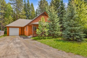 A log cabin with a garage, surrounded by dense forest.