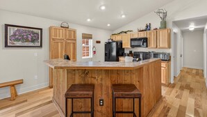 A kitchen with wooden cabinets, a central island with stools, a refrigerator, microwave, and a toaster. - Hubbard Cabin in McCall - near Payette Lake, private hot tub, quiet (McCall)