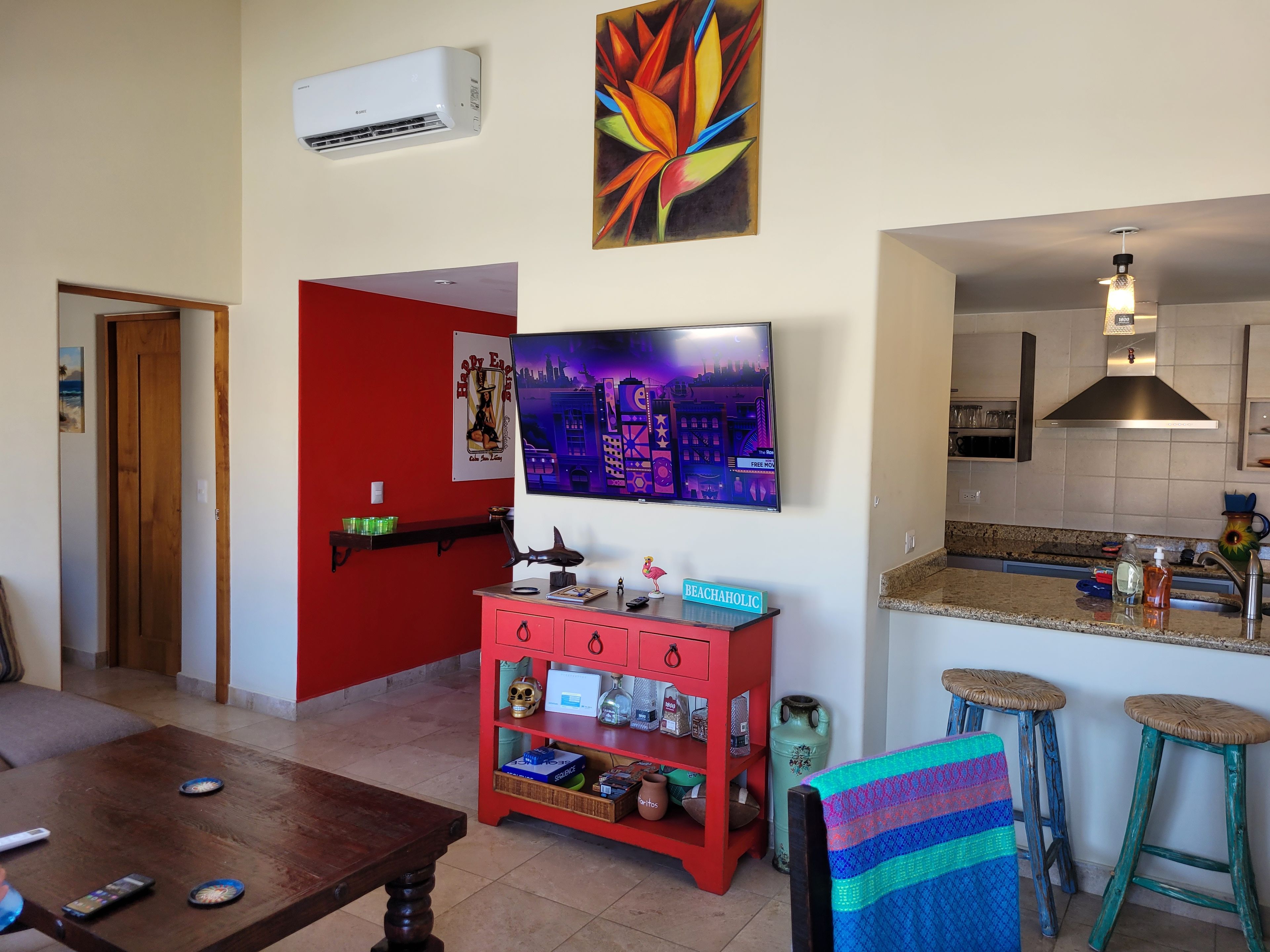 Een woonkamer met een televisie, een rode kast, een keukenhoek en een eettafel.