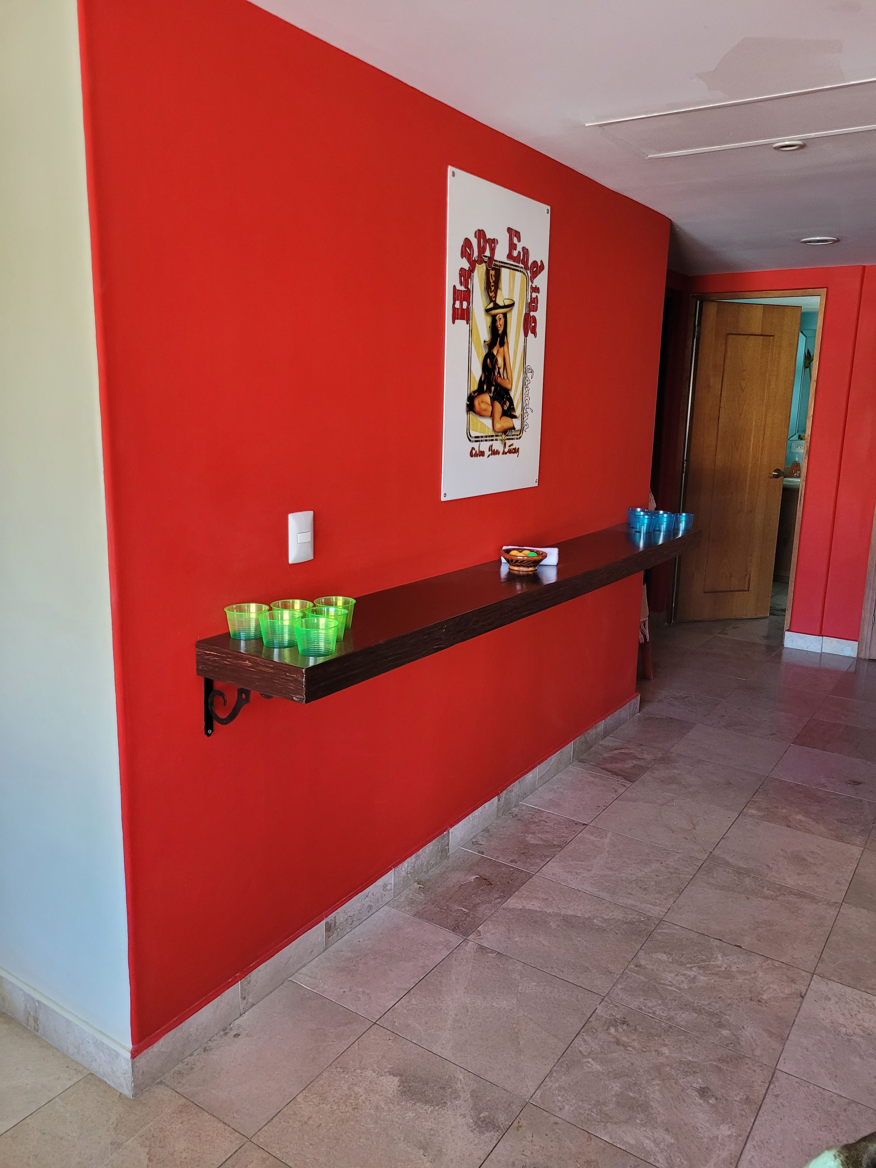 A hallway with a red wall, a poster, and a shelf with cups.