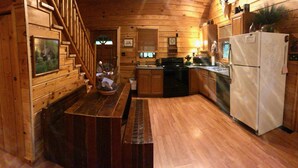 Una cucina in legno con una cabina, una scala in legno, un tavolo da pranzo, un frigorifero e un lavandino.