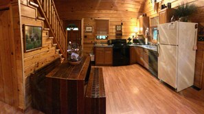 A wooden cabin kitchen with a wooden staircase, a dining table, a refrigerator, and a sink.