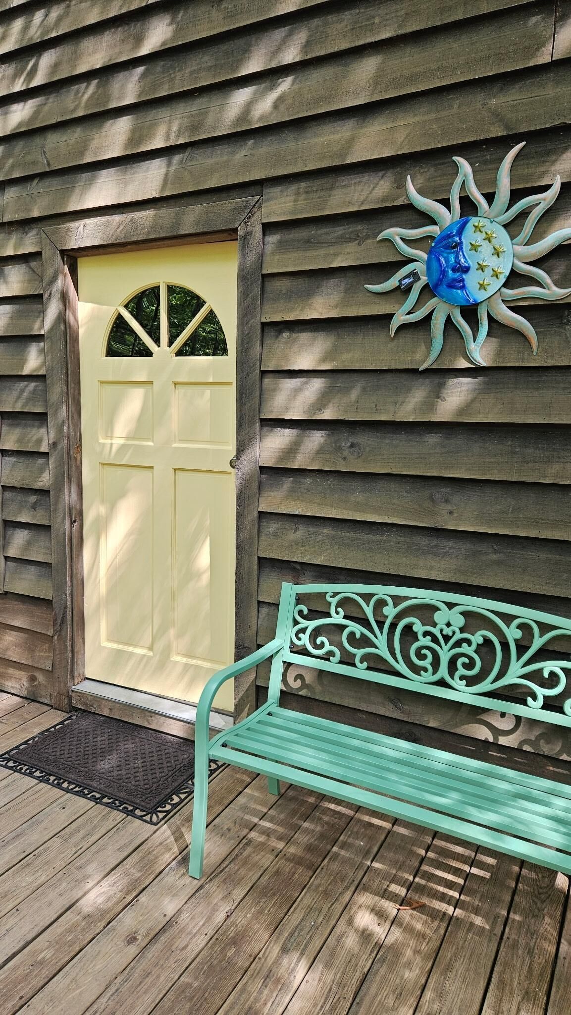 A wooden house with a yellow door, a decorative sun, and a green bench on the porch.