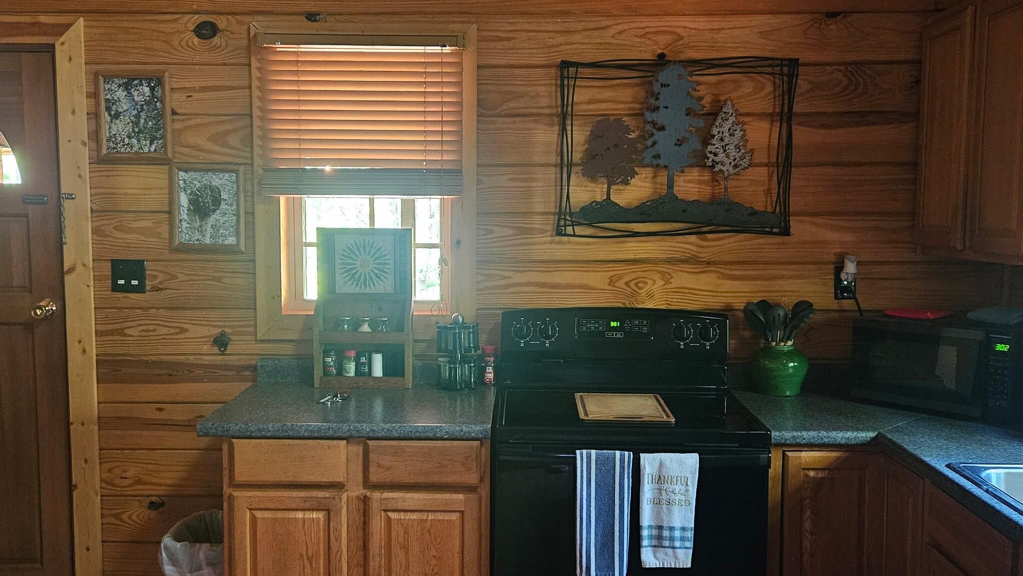Une cuisine avec des meubles de rangement en bois, une cuisinière, un four à micro-ondes et une fenêtre avec des stores.