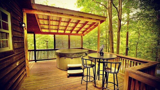 Un patio in legno con una vasca idromassaggio, due sgabelli da bar e un tavolo.