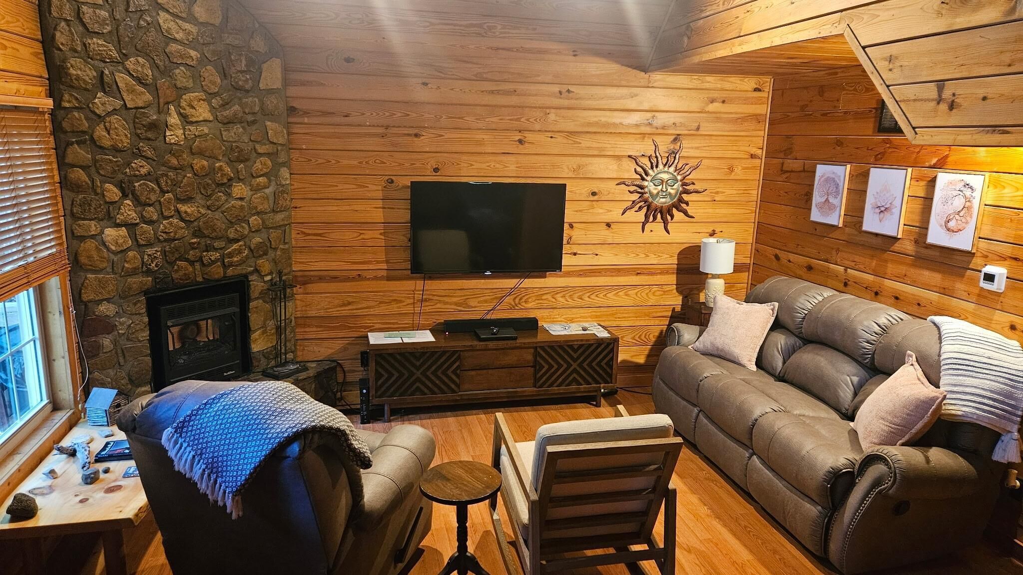 A cozy living room with a stone wall, wooden paneling, a flat-screen TV, a fireplace, and a sofa.