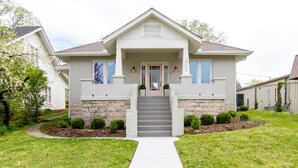 A two-story house with a front porch, a stone foundation, and a well-maintained lawn. - The Pink Door - 8th Ave Beauty - Stunning & Fresh (Nashville)