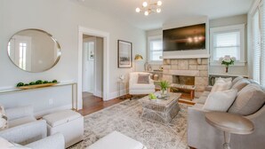 A modern living room with a fireplace, a large flat-screen TV, and a round mirror. - The Pink Door - 8th Ave Beauty - Stunning & Fresh (Nashville)