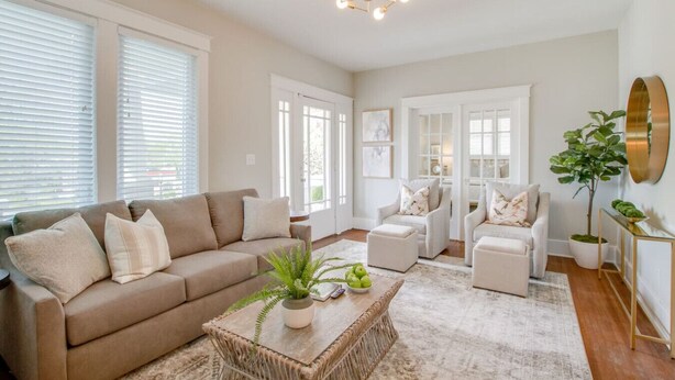 A spacious living room with a beige sofa, two armchairs, a coffee table with a plant, and a chandelier. - The Pink Door - 8th Ave Beauty - Stunning & Fresh (Nashville)