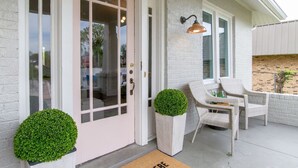 A white brick exterior with a pink door, two potted plants, and a patio area with wicker chairs and a table. - The Pink Door - 8th Ave Beauty - Stunning & Fresh (Nashville)