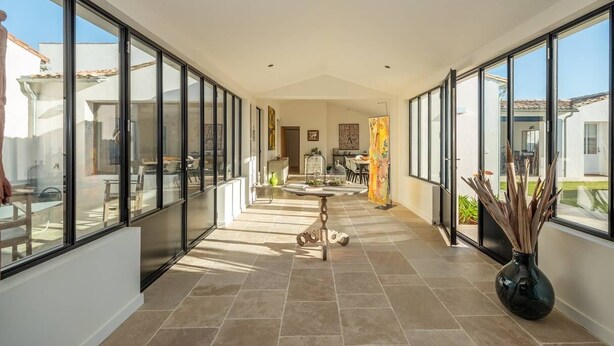 A spacious corridor with large windows, a central table, and a vase with plants. - Arte - Artist villa in the heart of la Noue (Sainte-Marie-de-Ré)