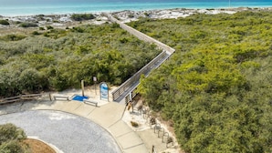 A coastal walkway with a wooden boardwalk, a blue sign, and a paved area with benches.