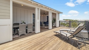 A covered outdoor deck with wicker furniture, a seating area, and a view of the surrounding landscape.