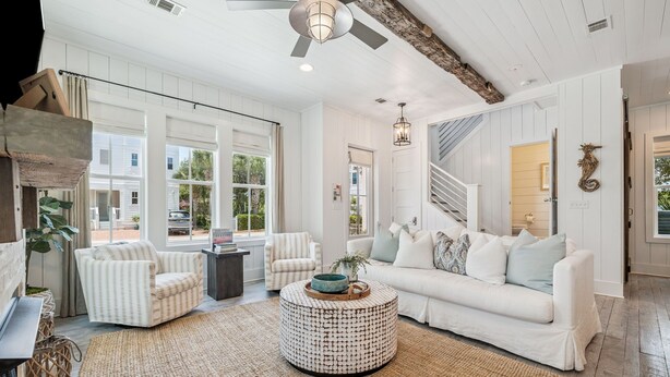 A spacious living room with a white sofa, striped armchairs, a round coffee table, and large windows offering a view of the outdoors.