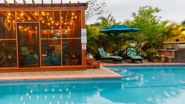 A pool area with a glass-enclosed structure, outdoor seating, and a tiled pool edge. - The Luxury Poolhouse, Casa 2 at Casa de Shelley   Corozal, Belize (Ranchito, Corozal)