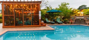 A pool area with a glass-enclosed structure, outdoor seating, and a tiled pool edge.