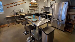 A modern kitchen with stainless steel appliances, a central island with bar stools, and overhead lighting. - Mountain Side Forest Retreat - Hot Tub!! - 1br 1ba <3beds> (Anchorage)