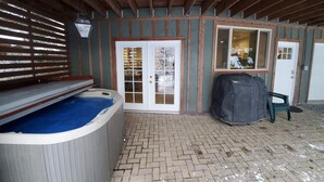A covered patio area with a hot tub, a covered grill, and a door leading to a garage. - Mountain Side Forest Retreat - Hot Tub!! - 1br 1ba <3beds> (Anchorage)