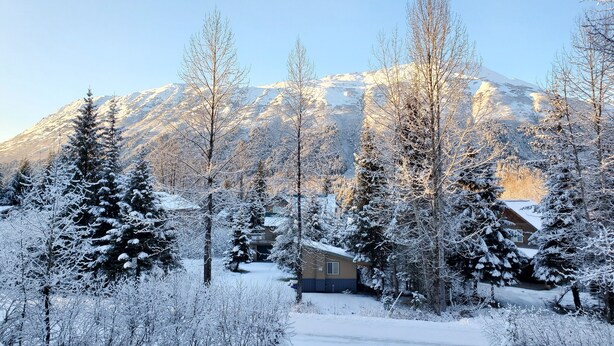 A snow-covered landscape with a mountain in the background and a house in the foreground. - Mountain Side Forest Retreat - Hot Tub!! - 1br 1ba <3beds> (Anchorage)