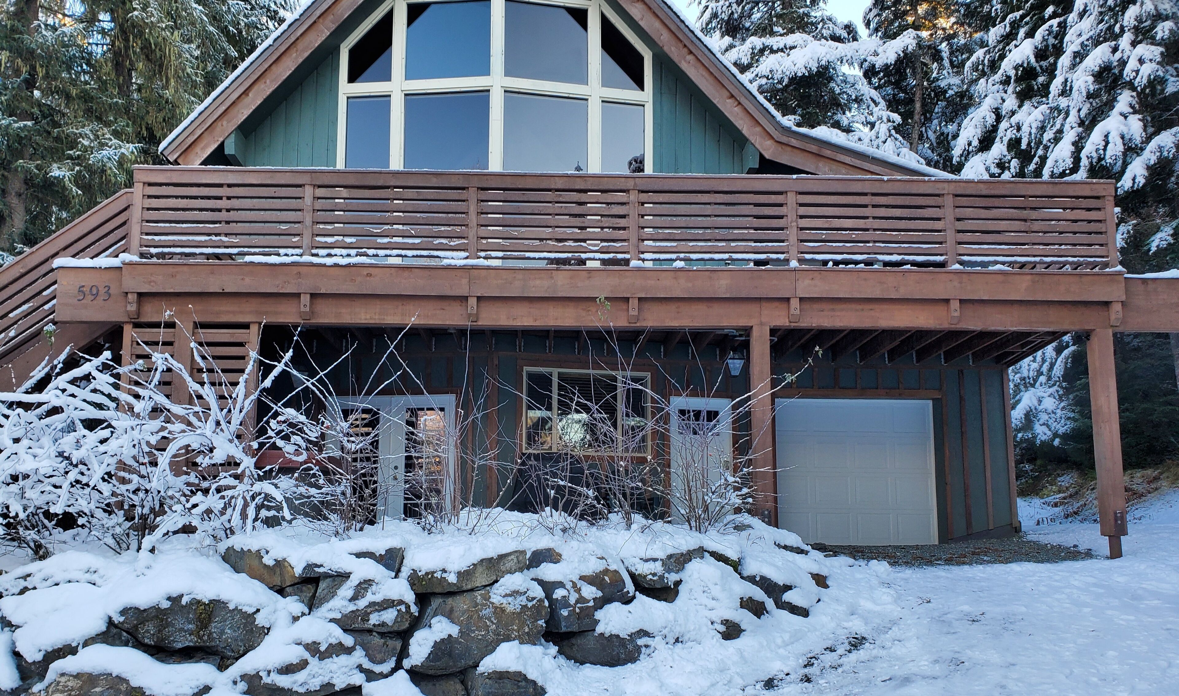A cabin with a wooden deck, a large window, and a garage.