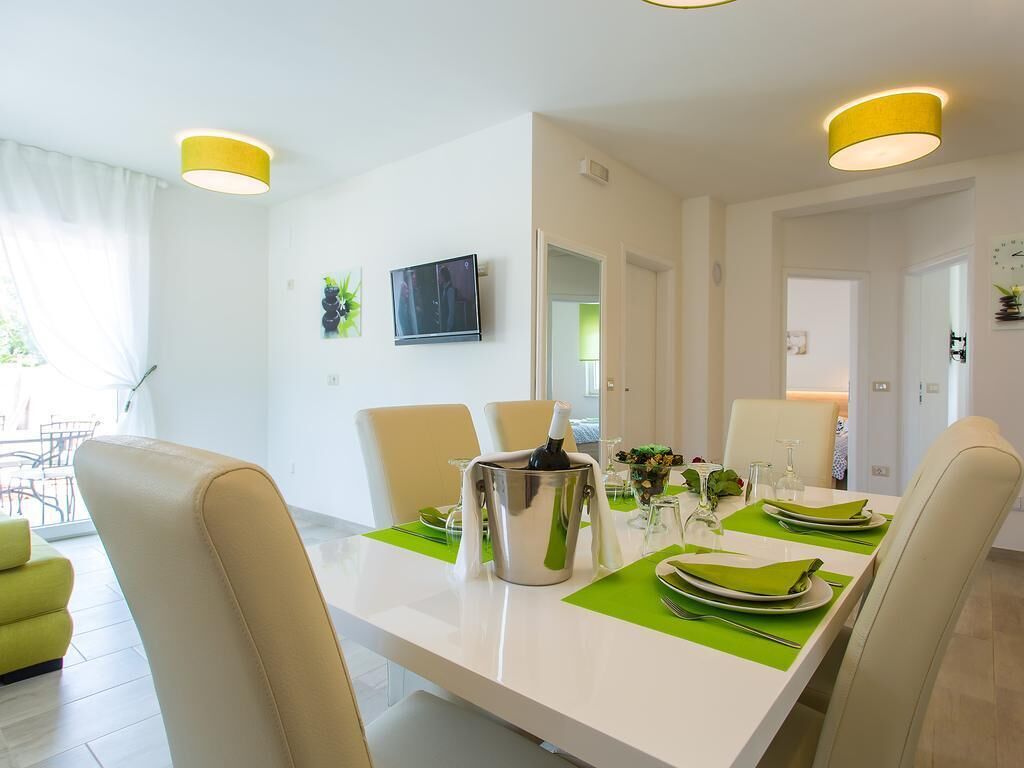 Een eetruimte met een witte tafel gedekt voor vier personen, groene placemats en een zilveren pot op tafel.
