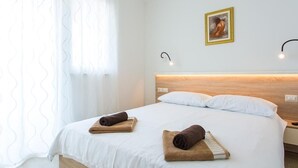 Ett hotellrum med en säng, två kuddar, en sänggavel, en tavla som hänger på väggen och en sänglampa.