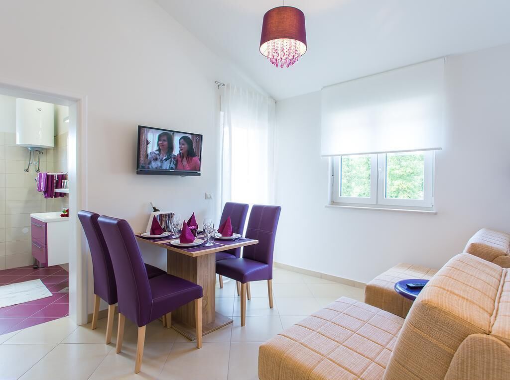 A modern living room with a dining area, a sofa, and a TV on the wall.