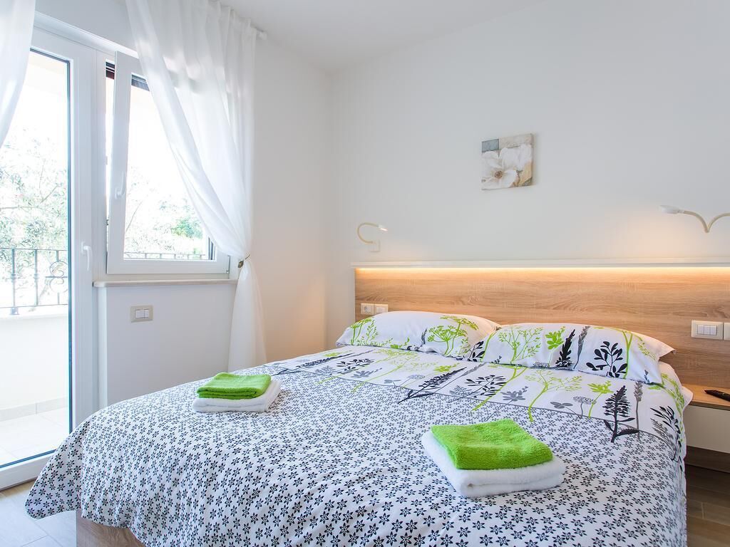 A hotel room with a bed, a window with curtains, a bedside table, and a wall-mounted light.
